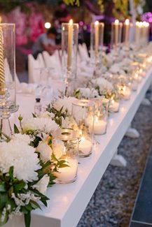 Μαγευτικός στολισμός γαμήλιου τραπεζιού με λευκά λουλούδια και ψηλά κηροπήγια