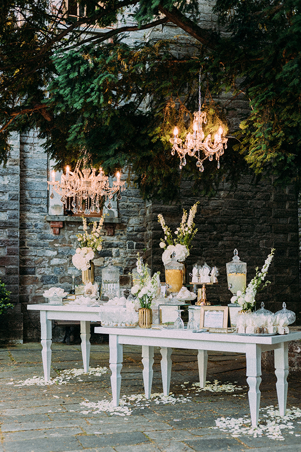 Λευκό dessert table με χρυσές βάσεις και λευκά λουλούδια