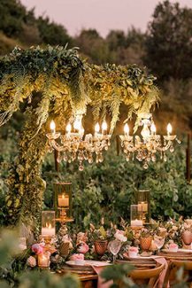 Μαγευτικός στολισμός γαμήλιου τραπεζιού με πλούσια γιρλάντα από πρασινάδα και κρεμαστούς πολυελαίους