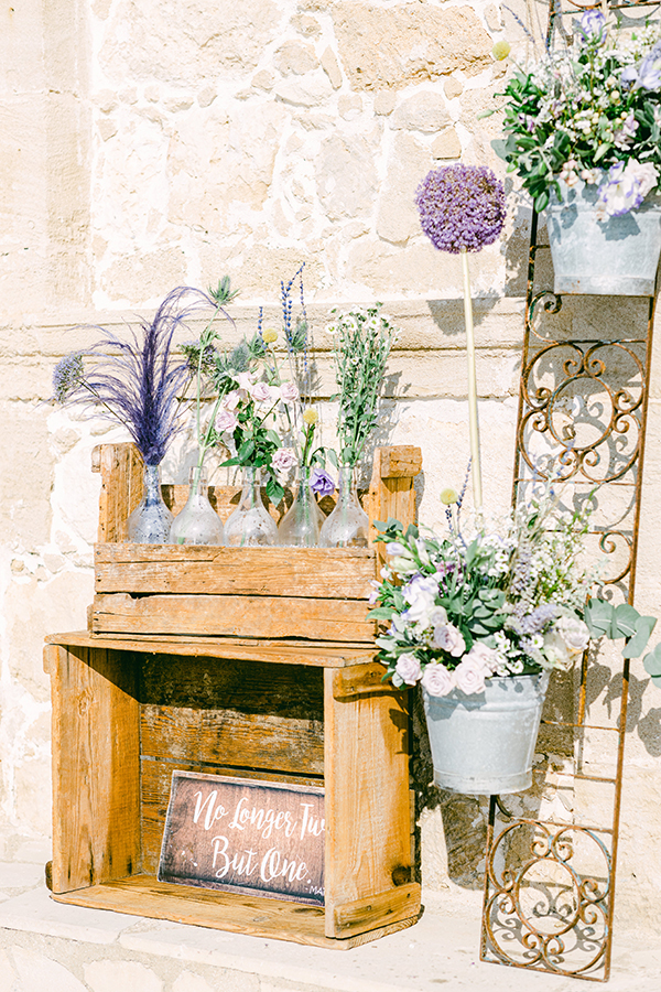 Ρουστίκ στολισμός εκκλησίας με ξύλινο στάντ και γυάλινα βάζα με άνθη σε μωβ αποχρώσεις