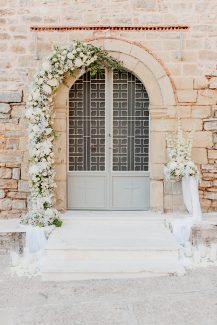 Λευκός στολισμός εισόδου εκκλησίας με υπέροχη γιρλάντα λουλουδιών και κεριά
