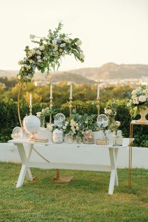 Ροματικός στολισμός dessert table με ημικύκλια λουλουδένια αψίδα και λευκά κεριά