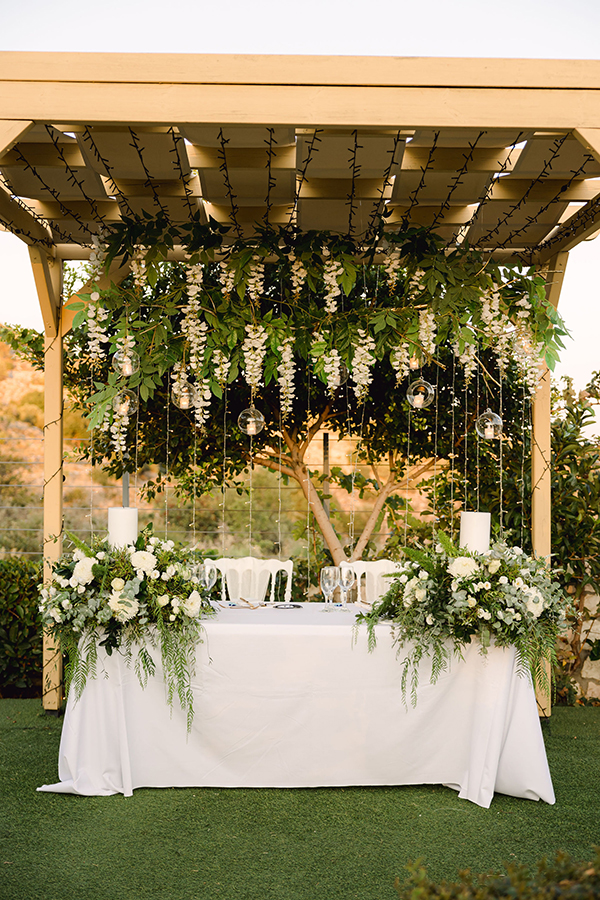Εντυπωσιακός στολισμός γαμήλιου τραπεζιού με κρεμαστή πρασινάδα και λευκά άνθη